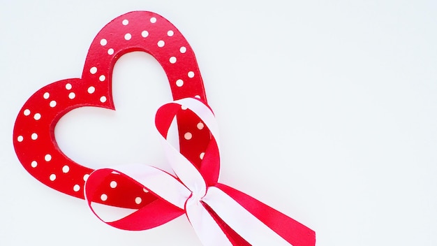 Valentines day concept Red wooden heart with white dots and ribbon bow on a stick White background A beautiful bow as a decoration Love and relationships Recognition or congratulations