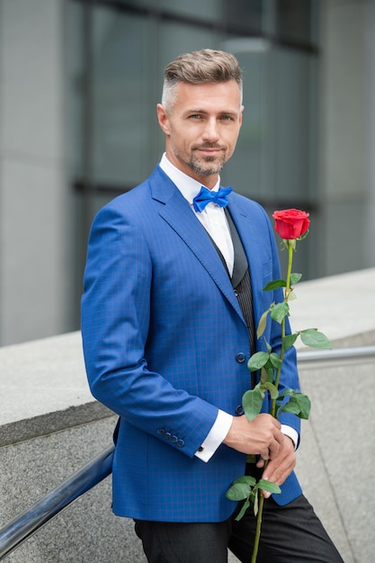 Valentines day concept smiling tuxedo man with valentines rose flower gift for valentines day