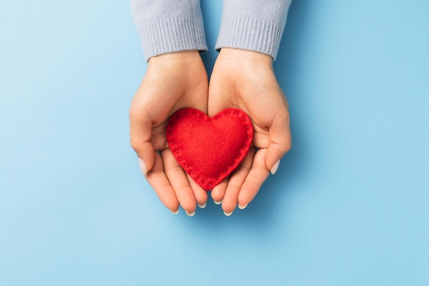 Concetto di san valentino con un cuore rosso nei palmi di una donna su sfondo blu