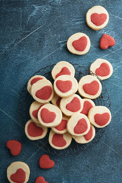 バレンタインデーのクッキー 暗い青色の背景にパーチメント紙に甘い赤いハートの中のショートブレッド クッキー 母の日 女性の日 甘い休日のベーキング トップ ビュー