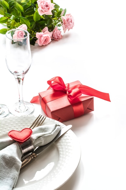 Valentines day dinner with table place setting with red gift, glass for champagne. Valentine's card.