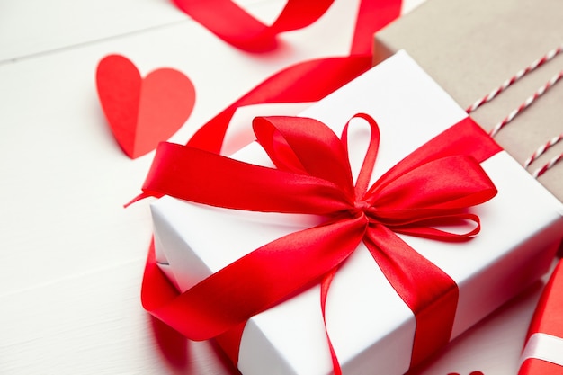 Valentines day gift box and red paper heart on white wooden background