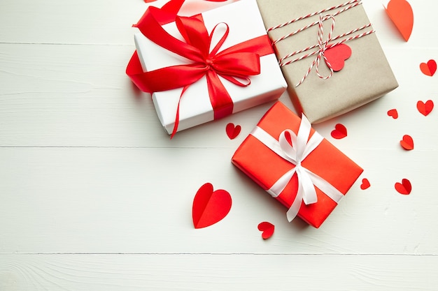 Valentines day gift boxes and red paper hearts on white wooden table