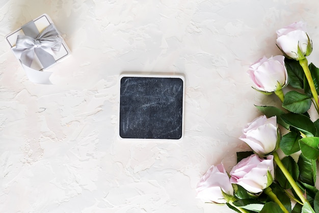 Valentines day greeting card. Pink roses and gift box with small chalk boards on light stone , Top view with copyspace