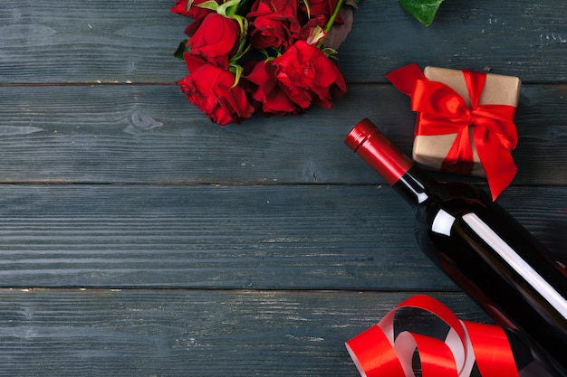 valentines day greeting card. red rose flowers, wine and gift box on wooden table.