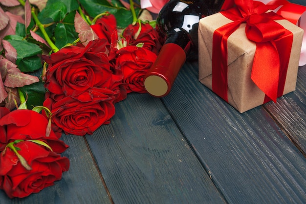 Valentines day greeting card. Red rose flowers, wine and gift box on wooden table.