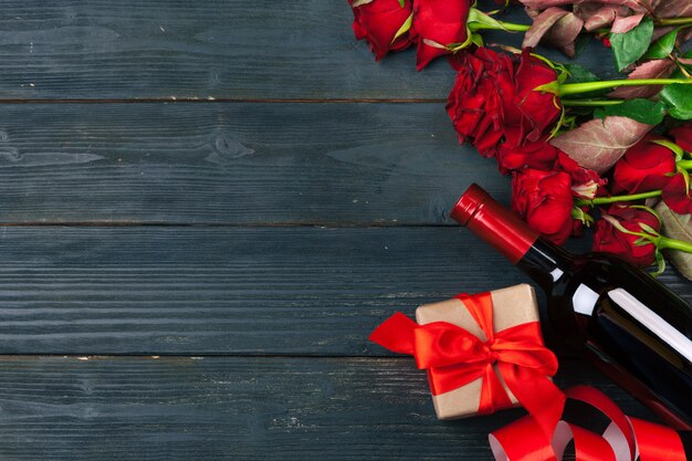 Поздравительная открытка дня валентинок, цветки красной розы, вино и подарочная коробка на деревянном столе.