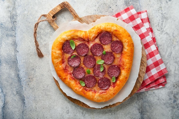 Valentines day heart shaped pizza with mozzarella pepperoni and basil wine bottle two wineglass gift box on light grey background Idea for romantic dinner Valentines day Top view Mock up