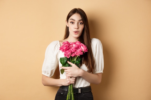 Valentines day. Image of surprised girlfriend thanking for flowers, receive pink roses from lover