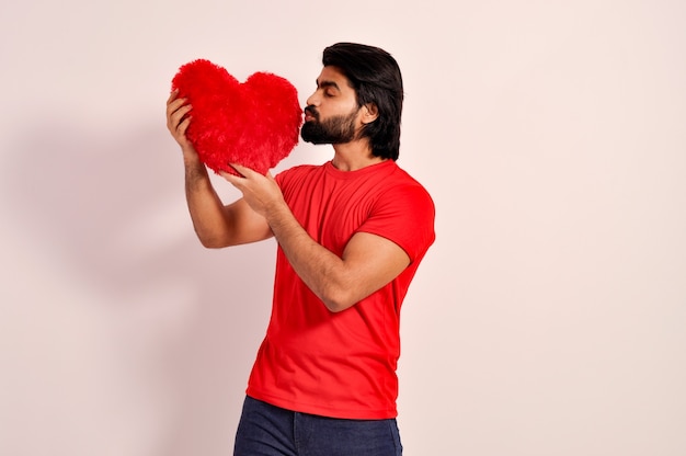 Valentines day Indian handsome young man holding and Kissing a red heart shaped pillow