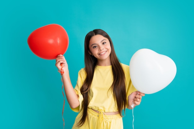 Valentines day and kids concept Teenage girl in yellow dress with red heartshaped balloon over blue background Happy girl face positive and smiling emotions