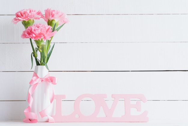 Valentines day and love concept. Pink carnation in vase on wooden background.