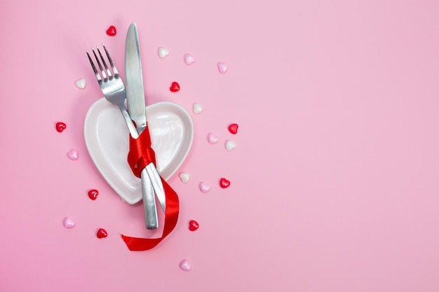 Valentines day meal background with red ribbon hearts fork knife white plate and napkin Romantic holiday table setting Beautiful background with blank Restaurant concept Flat lay High quality