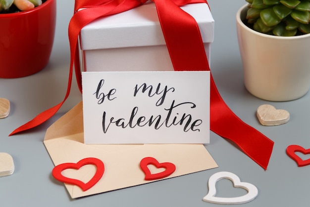 Valentines Day present with red bow and BE MY VALENTINE card close up on grey table