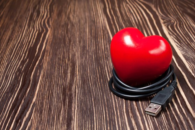 Foto cuore rosso di san valentino con cavo usb su fondo di legno marrone con spazio per testo. concetto di amore e tecnologia