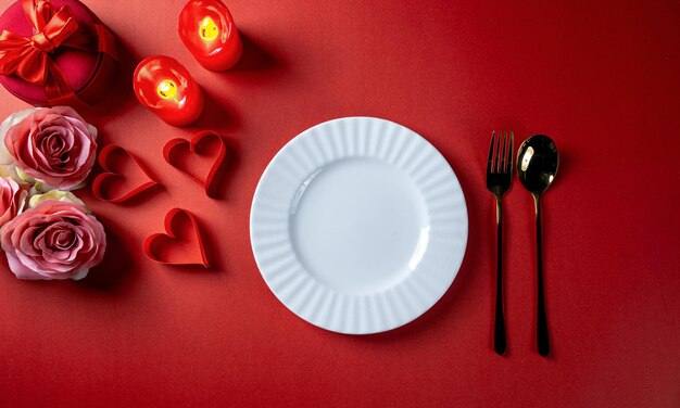 발렌타인 데이 빨간색 테마에는 흰색 빈 접시, 종이 하트, 촛불, 꽃, 선물 상자가 있습니다.