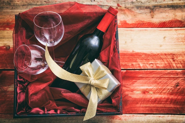 Valentines day Red wine bottle glasses and a gift in a box wooden background with copyspace