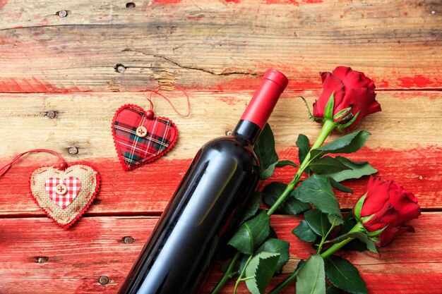 Valentines day red wine bottle and red roses on wooden background