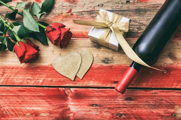 Valentines day Red wine bottle roses and a gift on wooden background