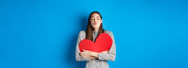 Valentines day romantic beautiful woman close eyes and pucker lips for kiss holding big red heart cu