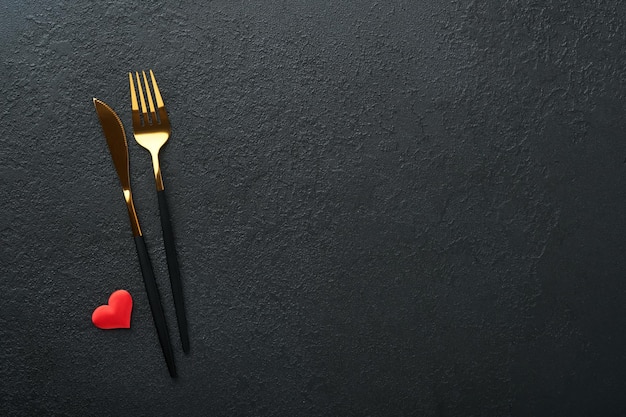 Valentines day romantic table setting Empty or closeup of a dinner black plate knife fork and decorative silk hearts on black background Holiday concept Copy space for inscriptions