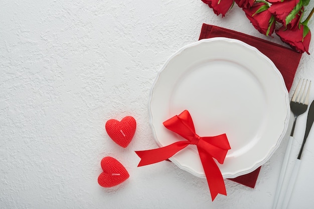 Valentines day romantic table setting Empty or closeup of a dinner black plate knife fork and decorative silk hearts on white background Holiday concept Copy space for inscriptions