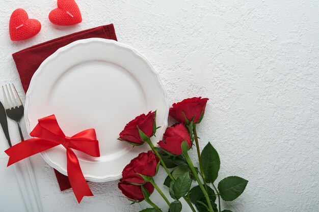 Valentines day romantic table setting Empty or closeup of a dinner black plate knife fork and decorative silk hearts on white background Holiday concept Copy space for inscriptions