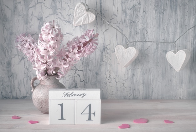 Valentines day still life with wooden calendar, pink hyacinth flowers and garland lights in shape of hearts