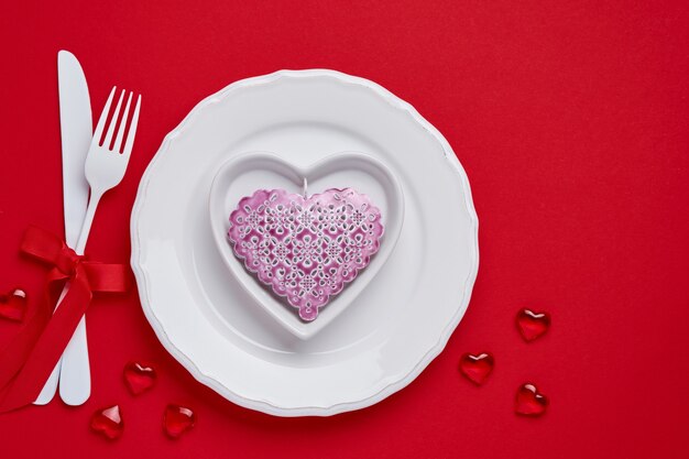 Valentines day table or concept with empty pink plate and whiteware on scarlet or red table. Top view flat lay with copy space.