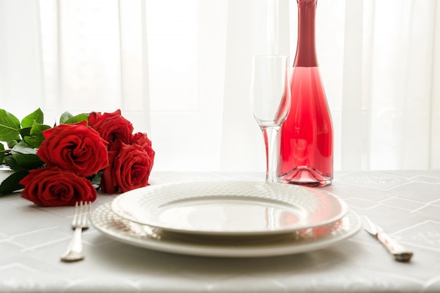 Valentines day table place setting with red roses and champagne. Invitation for a date.