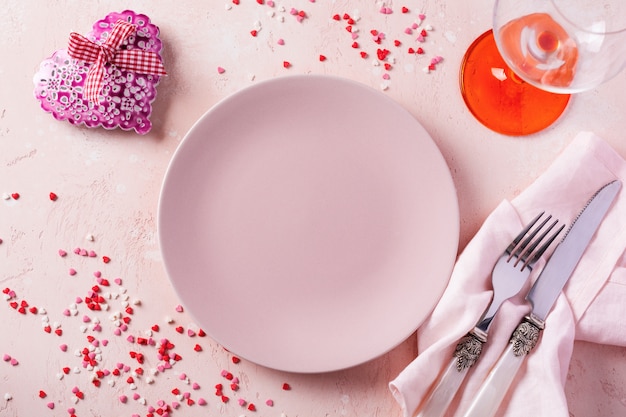 ピンクの明るい背景にピンクのプレートとギフトの心とバレンタインデーのテーブルの設定