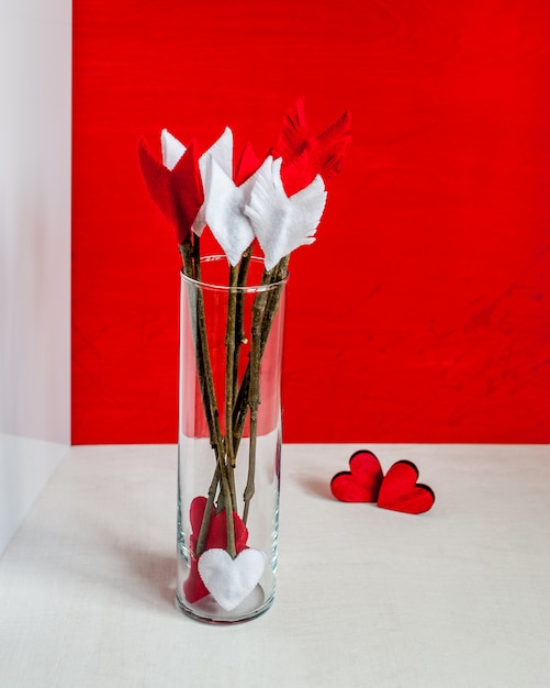 Valentines day twig arrows and hearts on red wooden background and glass vase. 