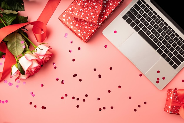 valentines day workspace with laptop keyboard, confetti, flowers and gift boxes