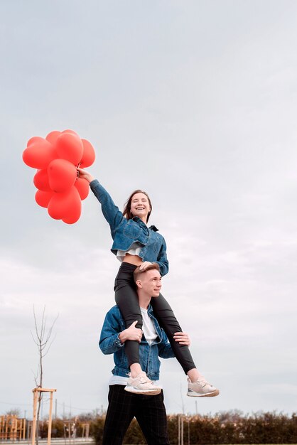 Valentines Day. Young loving couple hugging and holding red heart shaped balloons outdoors