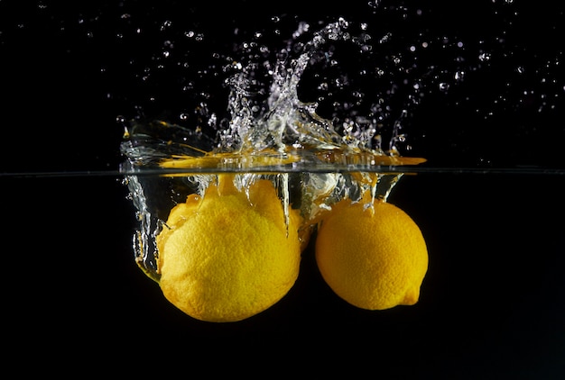 Vallende citroenen in water, spray voor ontwerp, bevriezing in beweging. Waterplons en groenten op een zwarte wordt geïsoleerd die