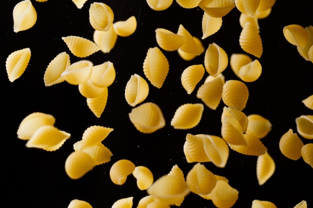 Vallende conchiglie pasta. Vliegende gele rauwe macaroni op zwarte achtergrond. Ondiepe DOF.