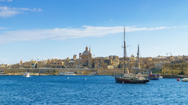 Valletta, malta - 27 november 2017 valletta ochtend skyline met basiliek van onze lieve vrouw van de berg karmel, middellandse zee met cruises antieke boot gezien vanaf sliema, malta.