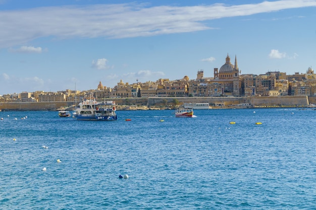 Valletta, malta - 27 november 2017 valletta ochtend skyline met basiliek van onze lieve vrouw van de berg karmel, middellandse zee met veerboot en antieke boten gezien vanaf sliema, malta.