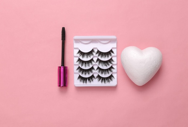 Valse wimpers met hart en wimpers penseel met mascara op roze achtergrond Creatief platte lay schoonheid concept