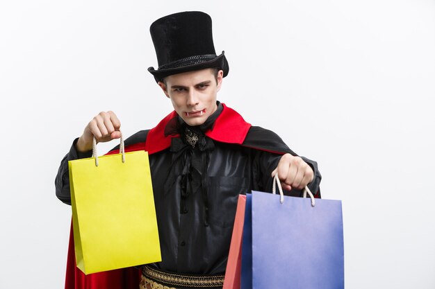 Vampire Halloween Concept - Happy handsome caucasian Vampire holding colorful shopping bag on white wall.