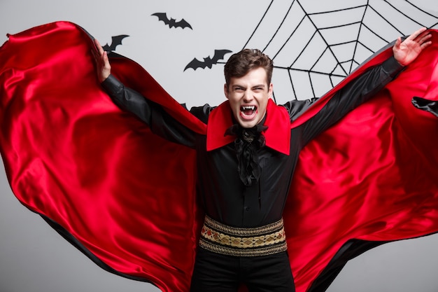 Vampire Halloween Concept - Portret van het knappe Kaukasisch Vampire Halloween-kostuum dat zijn rode, zwarte mantel fladdert.