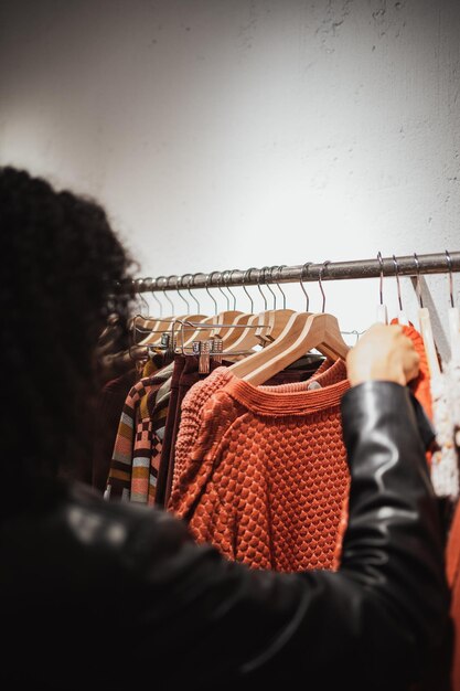 Van achteren geschoten van een jonge vrouw die een kleerhanger vasthoudt in een winkel