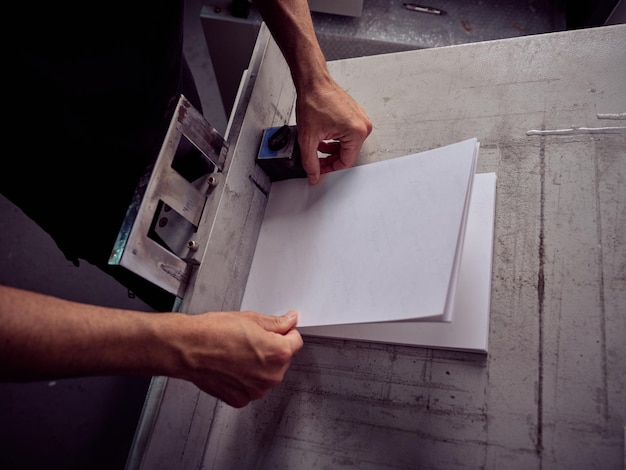 Van bovenaf een onherkenbare mannelijke ambachtsman die vellen papier op tafel legt terwijl hij in een professionele werkplaats werkt