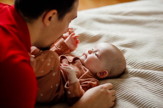 Van bovenaf gelukkige bebaarde man spelen en praten met schattige baby op comfortabel bed thuis