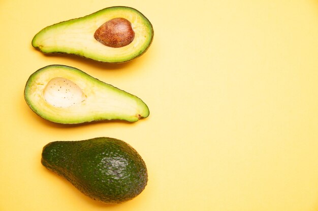 Van bovenaf van verse rijpe hele en gehalveerde avocado's met zaad gerangschikt op gele achtergrond