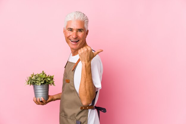 Van middelbare leeftijd tuinman man geïsoleerde punten met duim vinger weg, lachen en zorgeloos.