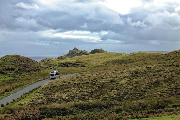 Van on road by field against cloudy sky