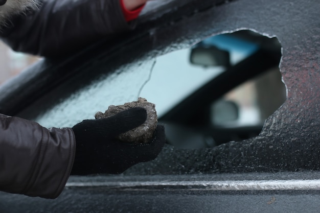 破壊行為の冬の男は車のガラスを小さな石を割った