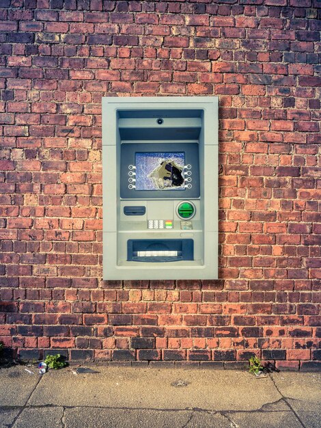 Photo a vandalized atm against a grungy red brick wall