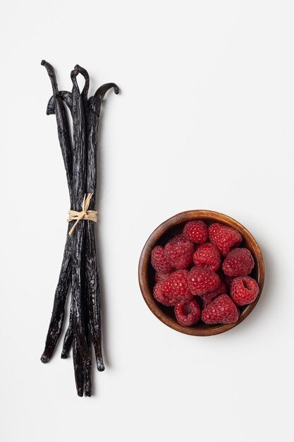 Vanilla beans with raspberries on white background